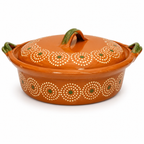 An orange glazed ceramic casserole dish with a matching lid, decorated with white circular dot patterns and small green accents, set against a plain white background.