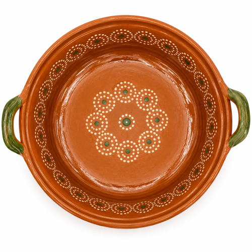 An overhead view of a round terracotta clay casserole dish with green handles and hand-painted white and green decorative patterns on the inside.