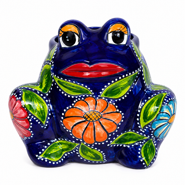A ceramic Mexican-style painted frog piggy bank on a white background. The frog's body is glossy dark blue, decorated with hand-painted green leaves, a large orange flower on the front, a red flower on the side, and smaller blue and orange flowers.