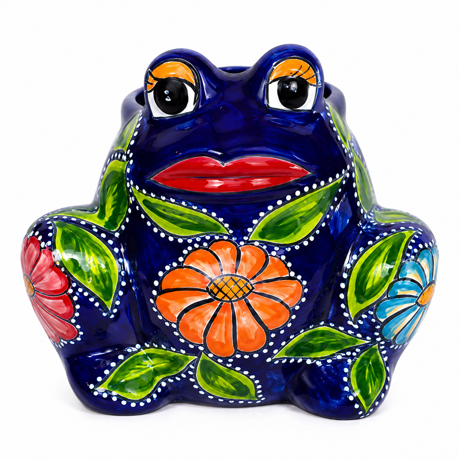 A ceramic Mexican-style painted frog piggy bank on a white background. The frog's body is glossy dark blue, decorated with hand-painted green leaves, a large orange flower on the front, a red flower on the side, and smaller blue and orange flowers.