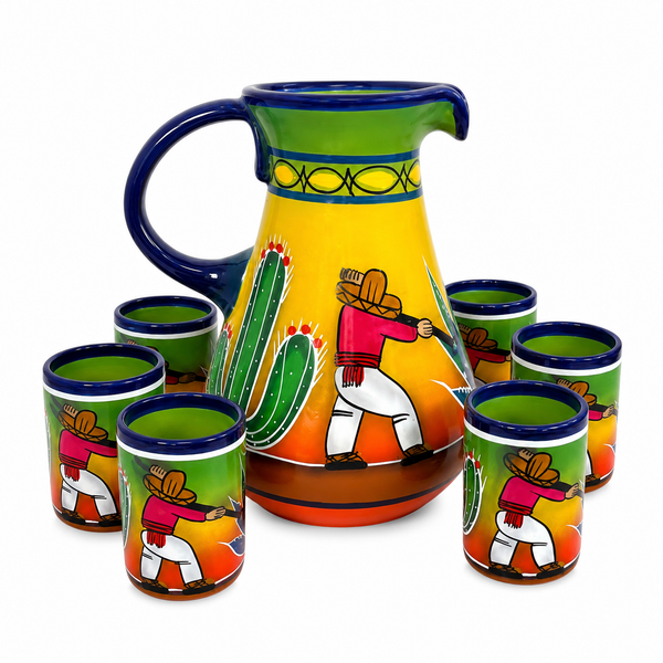 A hand-painted ceramic pitcher and matching shot glasses set on a white background. The set features a large pitcher and five shot glasses decorated with a vibrant Mexican desert scene, including a cactus, a cowboy, and a green sky.