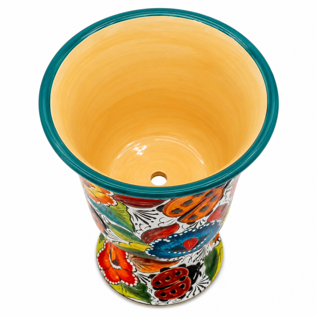 A hand-painted ceramic planter pot with a vibrant Mexican-style floral pattern in red, orange, blue, green, and yellow, featuring a solid yellow-orange glazed interior and a teal rim.