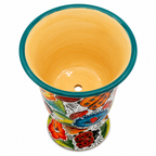 A hand-painted ceramic planter pot with a vibrant Mexican-style floral pattern in red, orange, blue, green, and yellow, featuring a solid yellow-orange glazed interior and a teal rim.