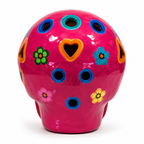 A glossy ceramic skull-shaped container or vase in bright pink, decorated with colorful floral and geometric cutout details in blue, green, yellow, orange, and pink on a white background.