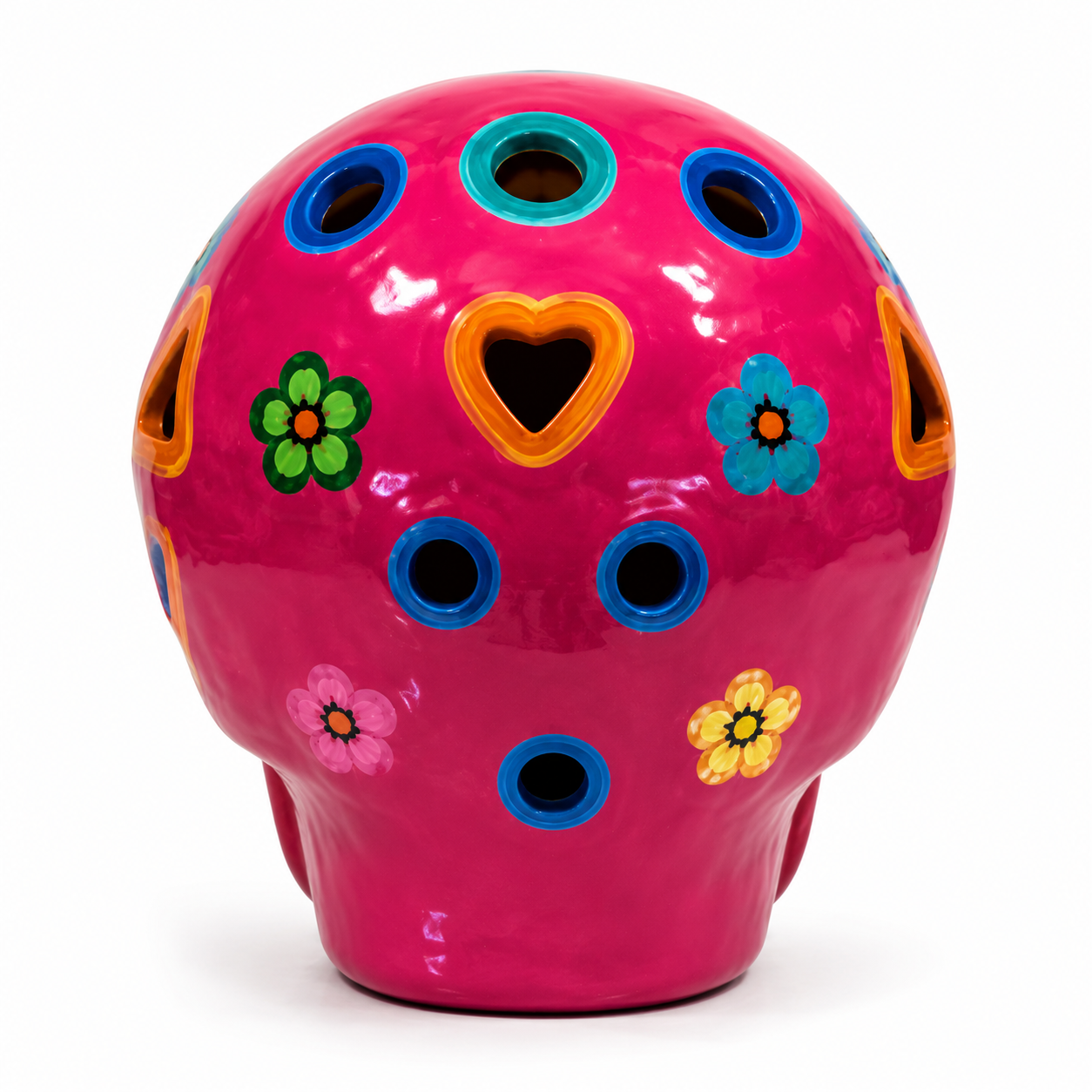 A glossy ceramic skull-shaped container or vase in bright pink, decorated with colorful floral and geometric cutout details in blue, green, yellow, orange, and pink on a white background.