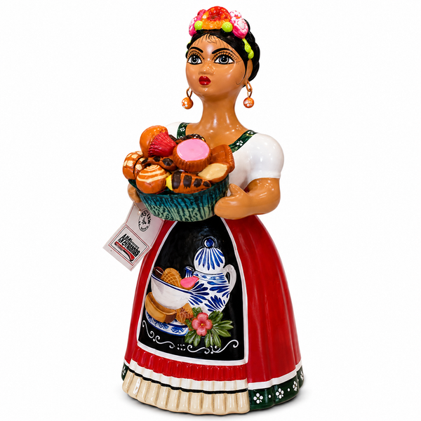 A ceramic Mexican-style figurine of a woman in traditional dress holding a basket of fruit and bread, with a visible hanging tag, photographed on a plain white background.
