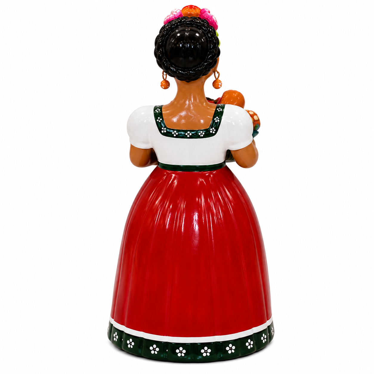 A ceramic Mexican folk saint figurine of Our Lady of Guadalupe shown from the back, wearing a red skirt, white blouse, and green floral trim, with dark hair and orange earrings, on a white background.